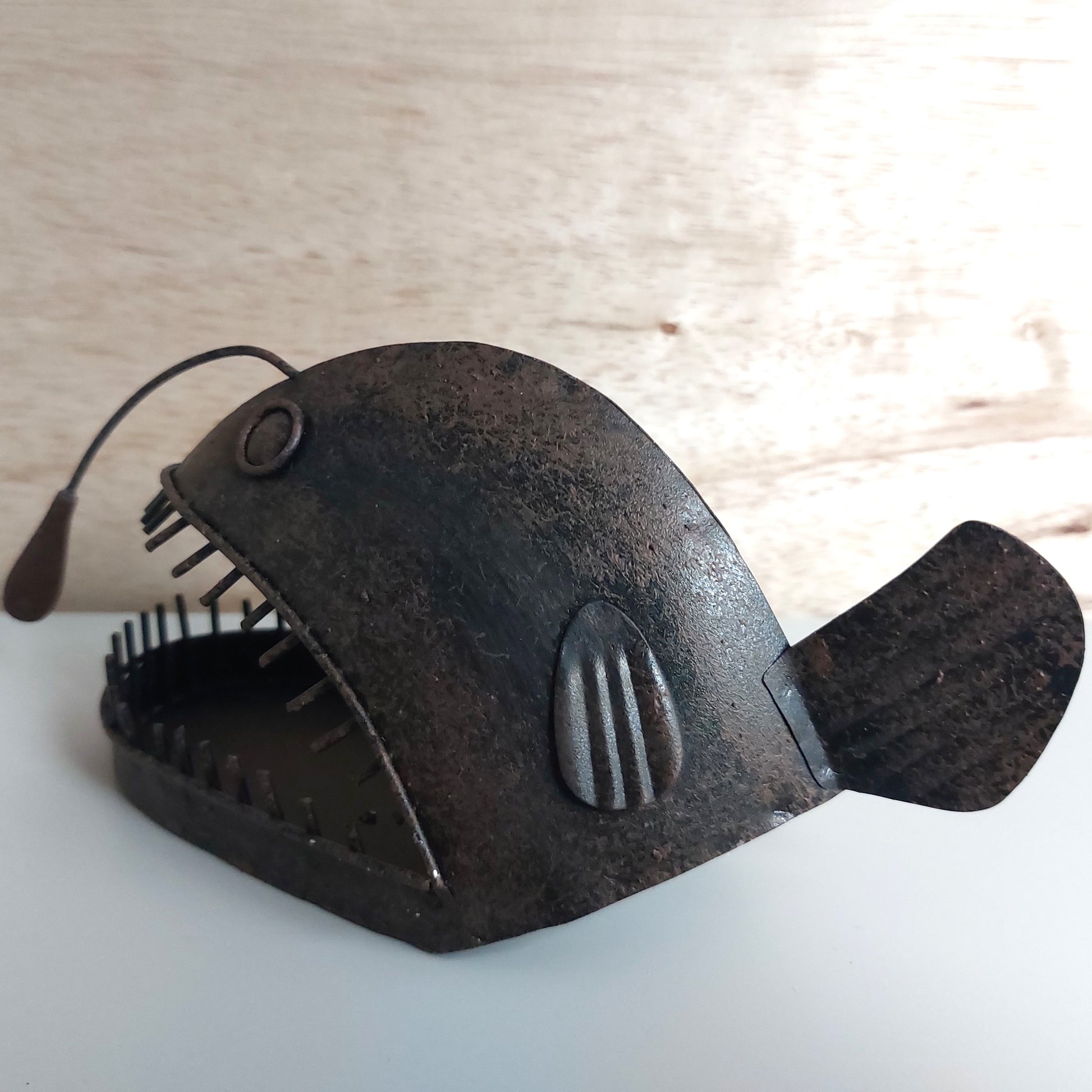 Decorative angler fish shaped object with a pointy mouth full of teeth on a light wooden surface