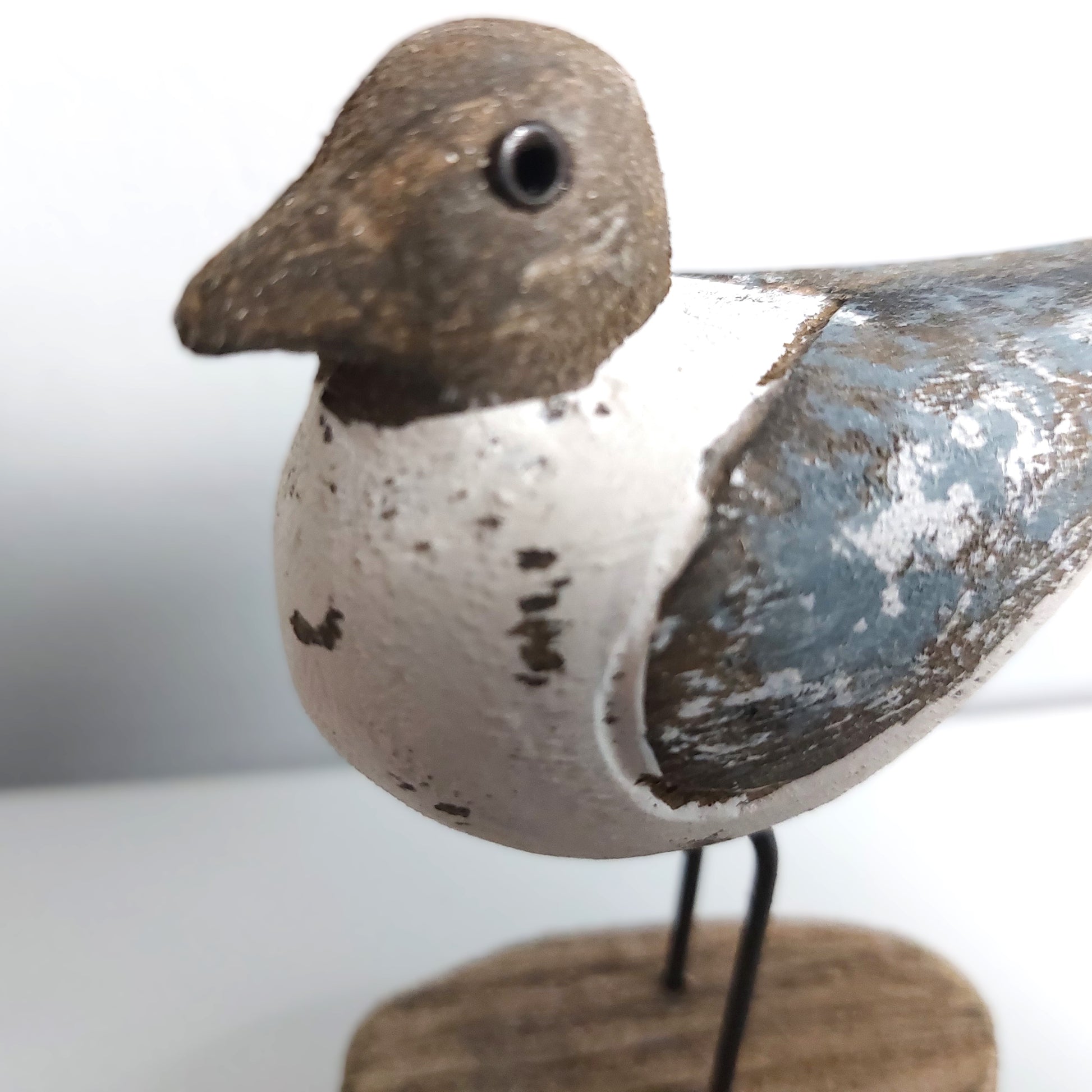 Close up of a Sanderling Wooden bird figurine with a white body, brown head, and blue wing on a stand against a light background.