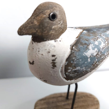 Close up of a Sanderling Wooden bird figurine with a white body, brown head, and blue wing on a stand against a light background.