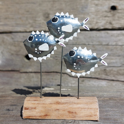 Three metal puffer fish sculptures on a wooden base against a wooden background