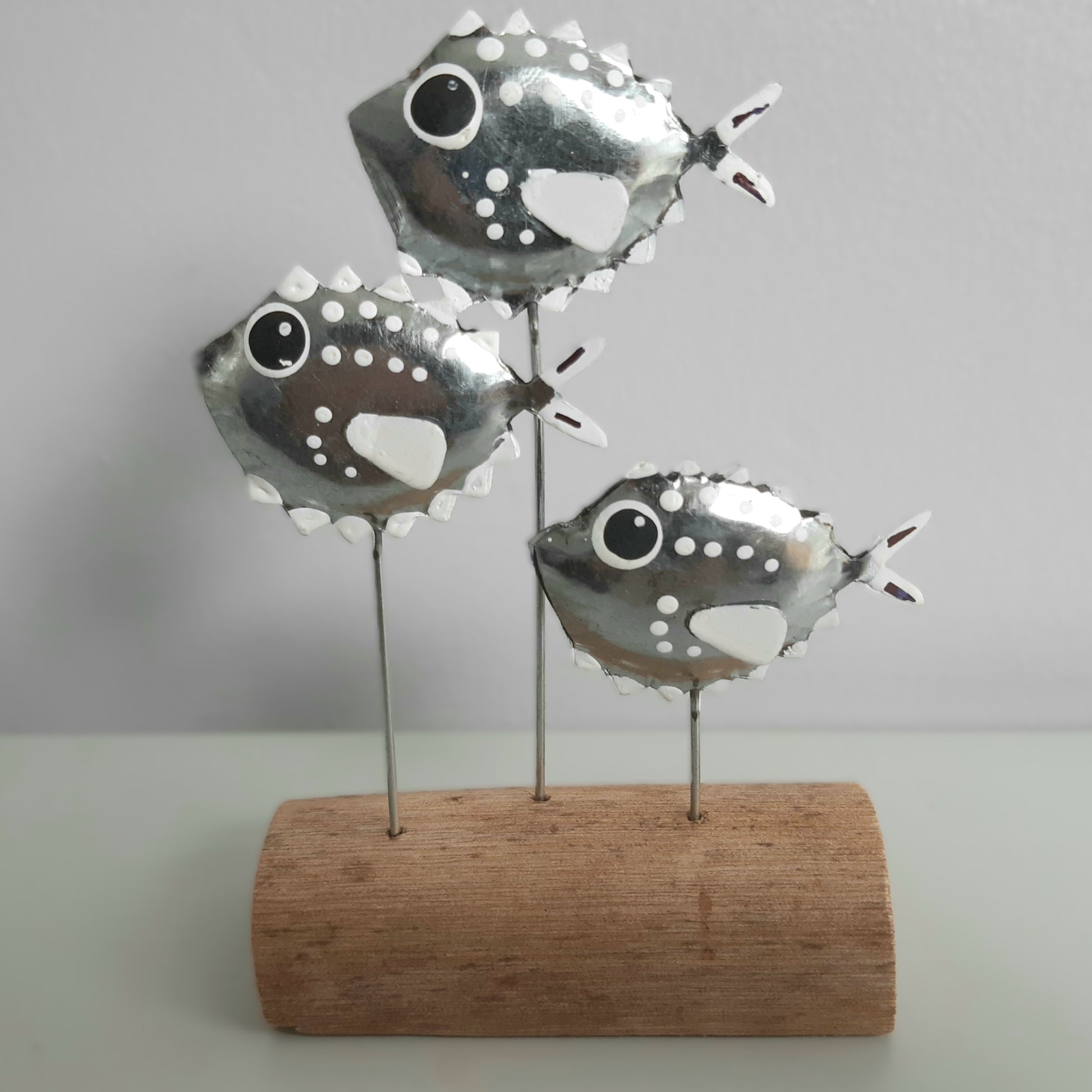 Decorative metal fish sculpture on a wooden base against a plain background