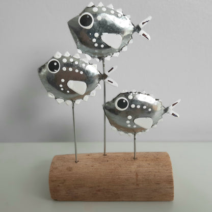Decorative metal fish sculpture on a wooden base against a plain background