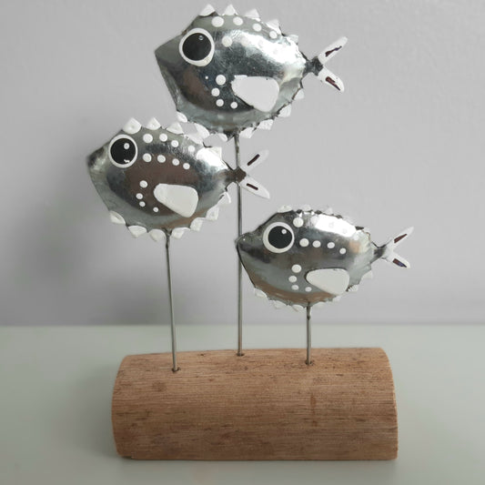 Decorative metal fish sculpture on a wooden base against a plain background
