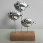 Decorative metal fish sculpture on a wooden base against a plain background
