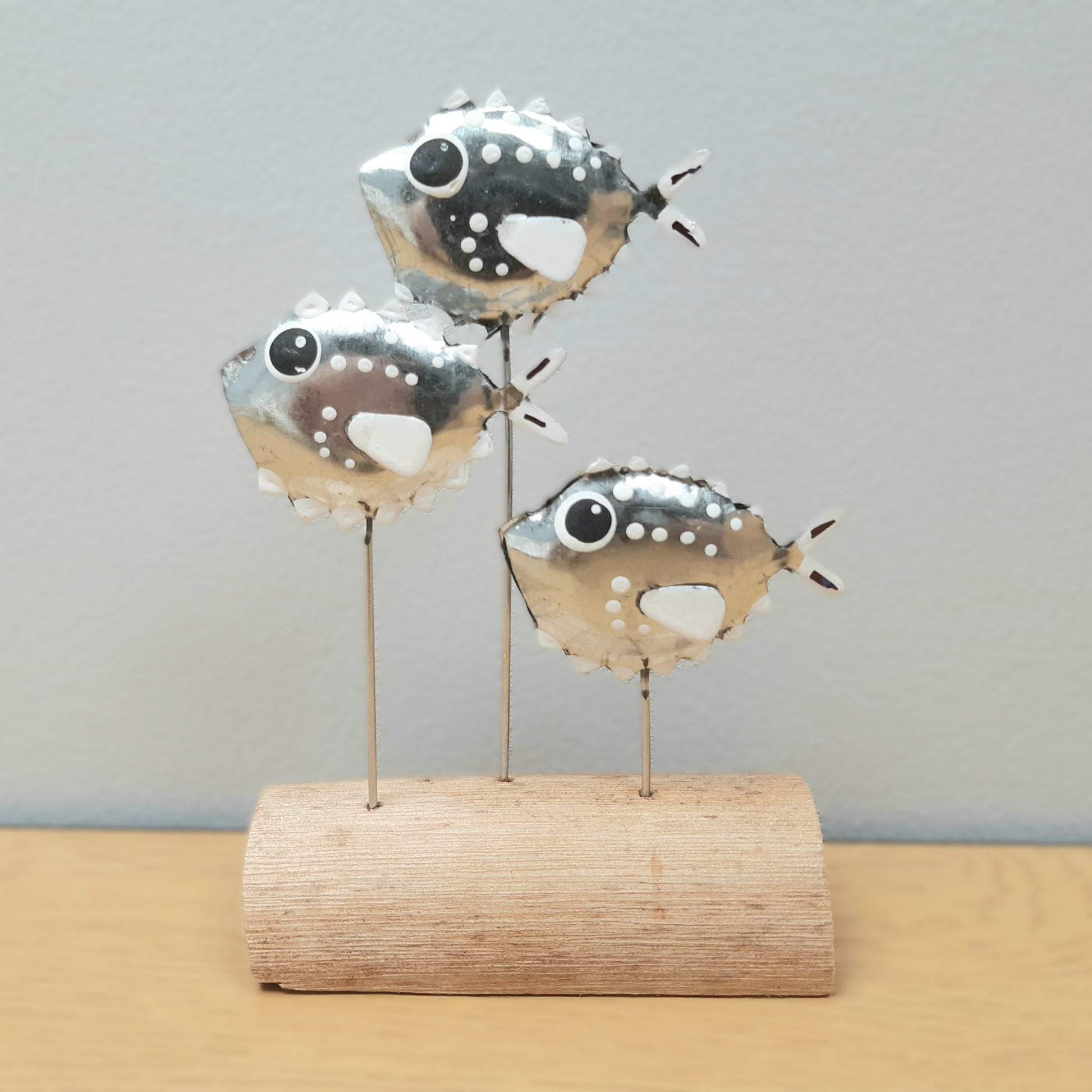 Decorative metal fish sculpture on a wooden base against a gray background