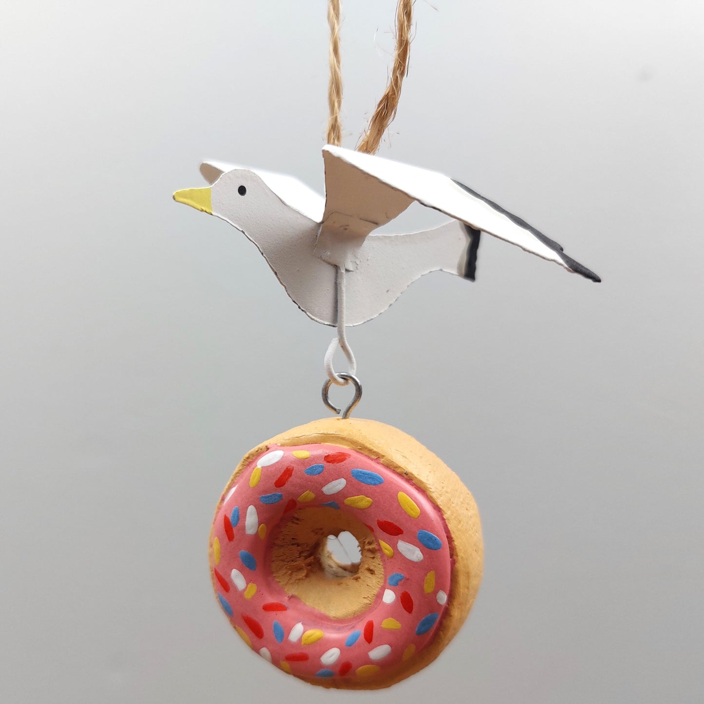 Decorative hanging ornament of a bird and a donut with pink icing and sprinkles on a gray background