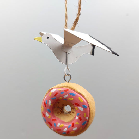 Decorative hanging ornament of a bird and a donut with pink icing and sprinkles on a gray background