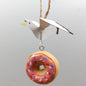 Decorative hanging ornament of a bird and a donut with pink icing and sprinkles on a gray background