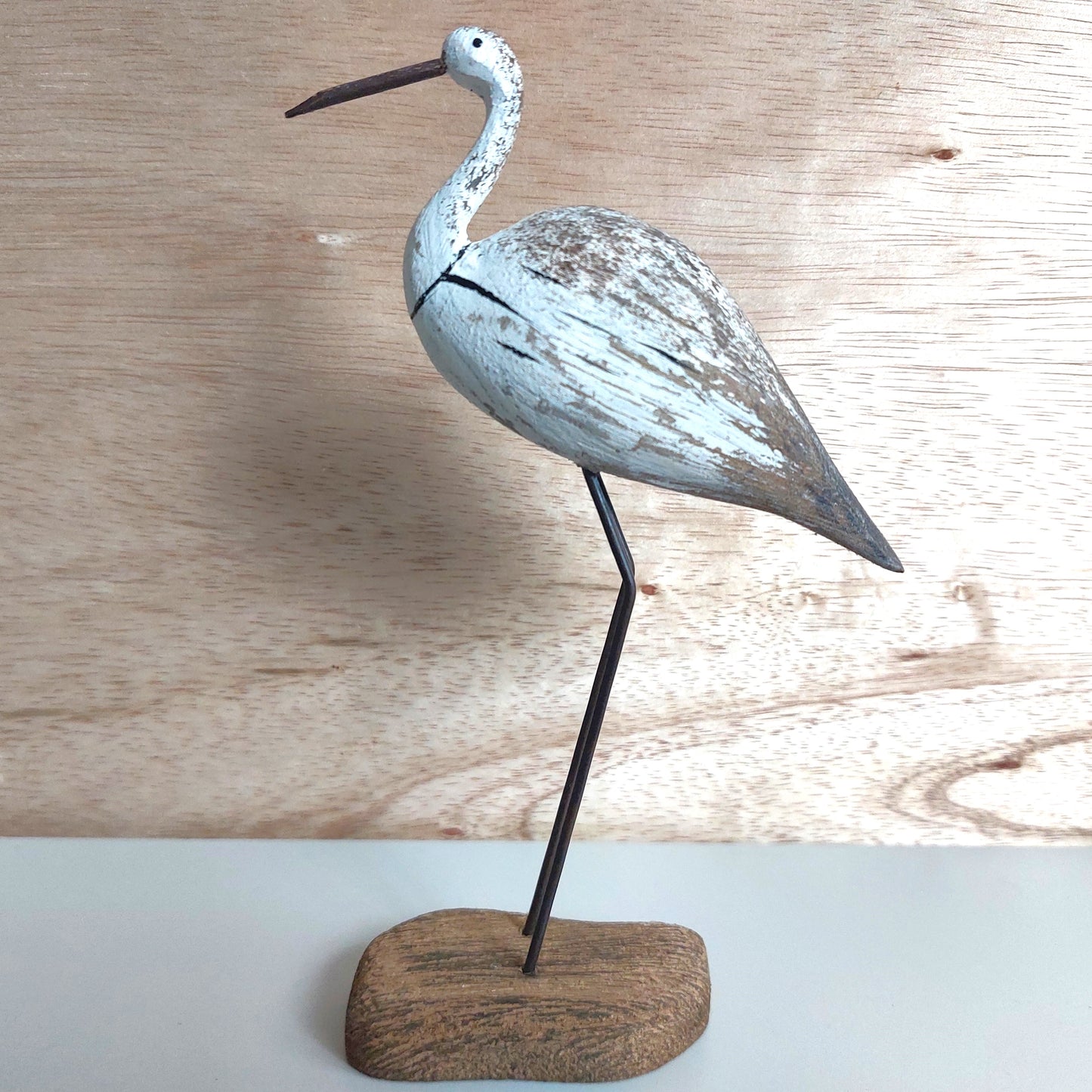 A wooden figurine of a tall wading bird on a wooden block against a wooden background