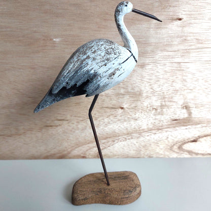 Wooden bird sculpture on a stand against a wooden background