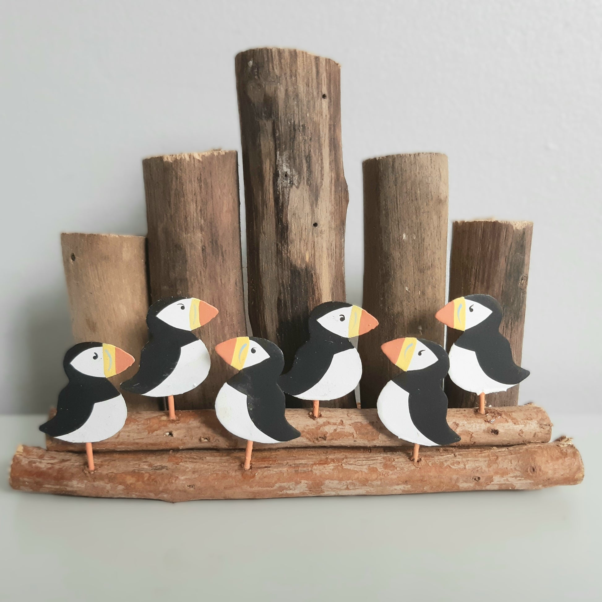 Decorative set of puffin figures on a wooden base with groyne logs in the background.