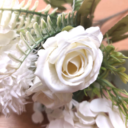 Ivory faux rose artificial flower with green leaves and stems, photographed close-up on a warm beige background.