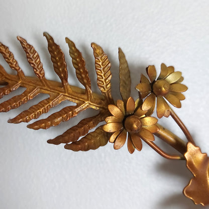 A close up of bronze style metal leaves and flowers against a pale background