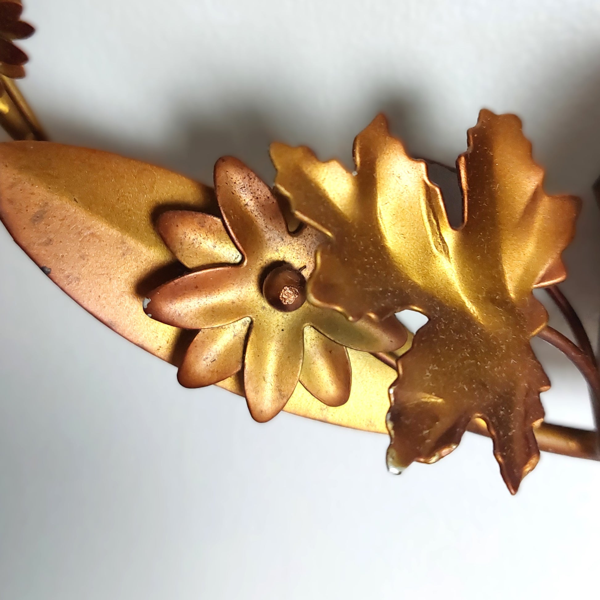 A close up of bronzed tin metal leaves and flowers against a pale background