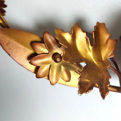 A close up of bronzed tin metal leaves and flowers against a pale background