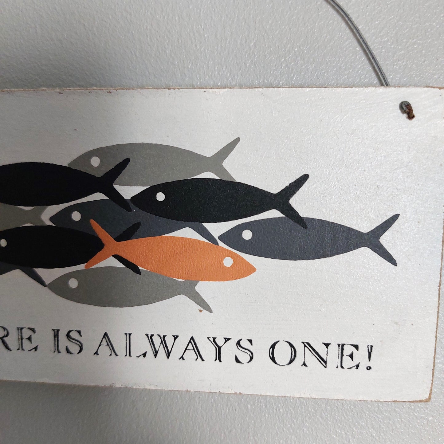 A rectangular white decorative sign featuring stylized fish in black, gray, and orange, with the text 'RE IS ALWAYS ONE!' in black lettering, shown hanging against a light wall.