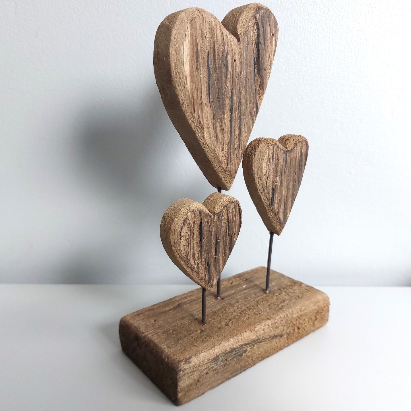 Wooden triple heart-shaped sculpture on a stand with a plain background