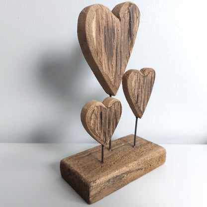 Wooden triple heart-shaped sculpture on a stand with a plain background