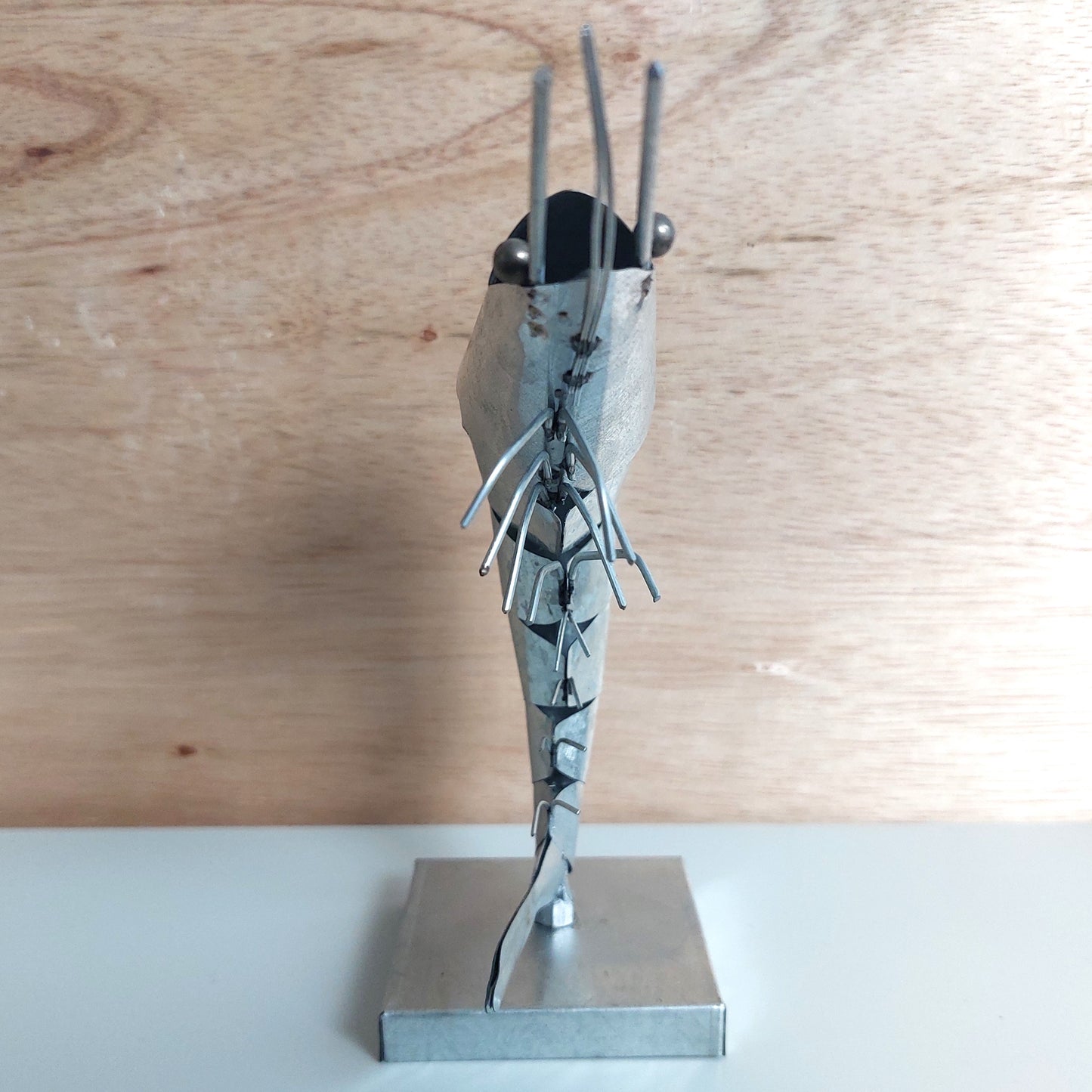 Metallic sculpture of a prawn on a wooden surface