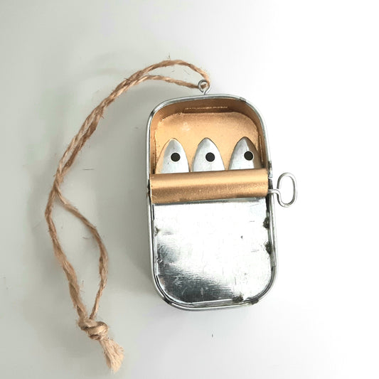 Metallic tin of 3 sardines peering out on a white background