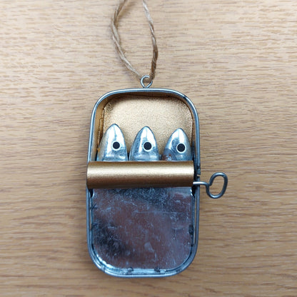Decorative metal tin with three metal sardine fish on a wooden surface