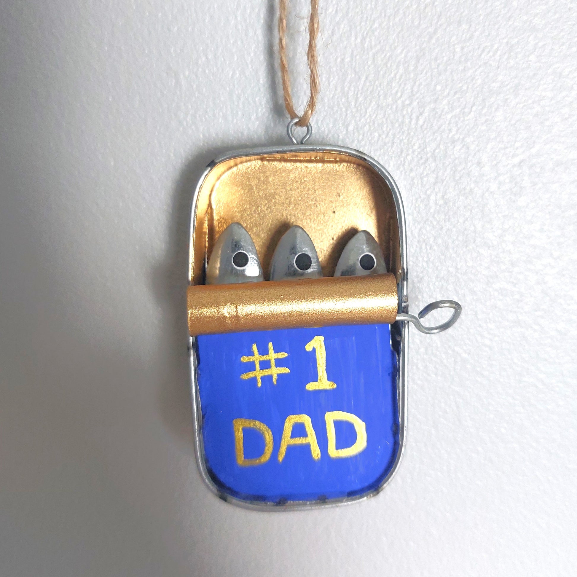 A hand painted small metal tin hanging decoration with metal sardines laying inside with a #1 Dad marking on the front of the tin