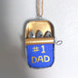 A hand painted small metal tin hanging decoration with metal sardines laying inside with a #1 Dad marking on the front of the tin