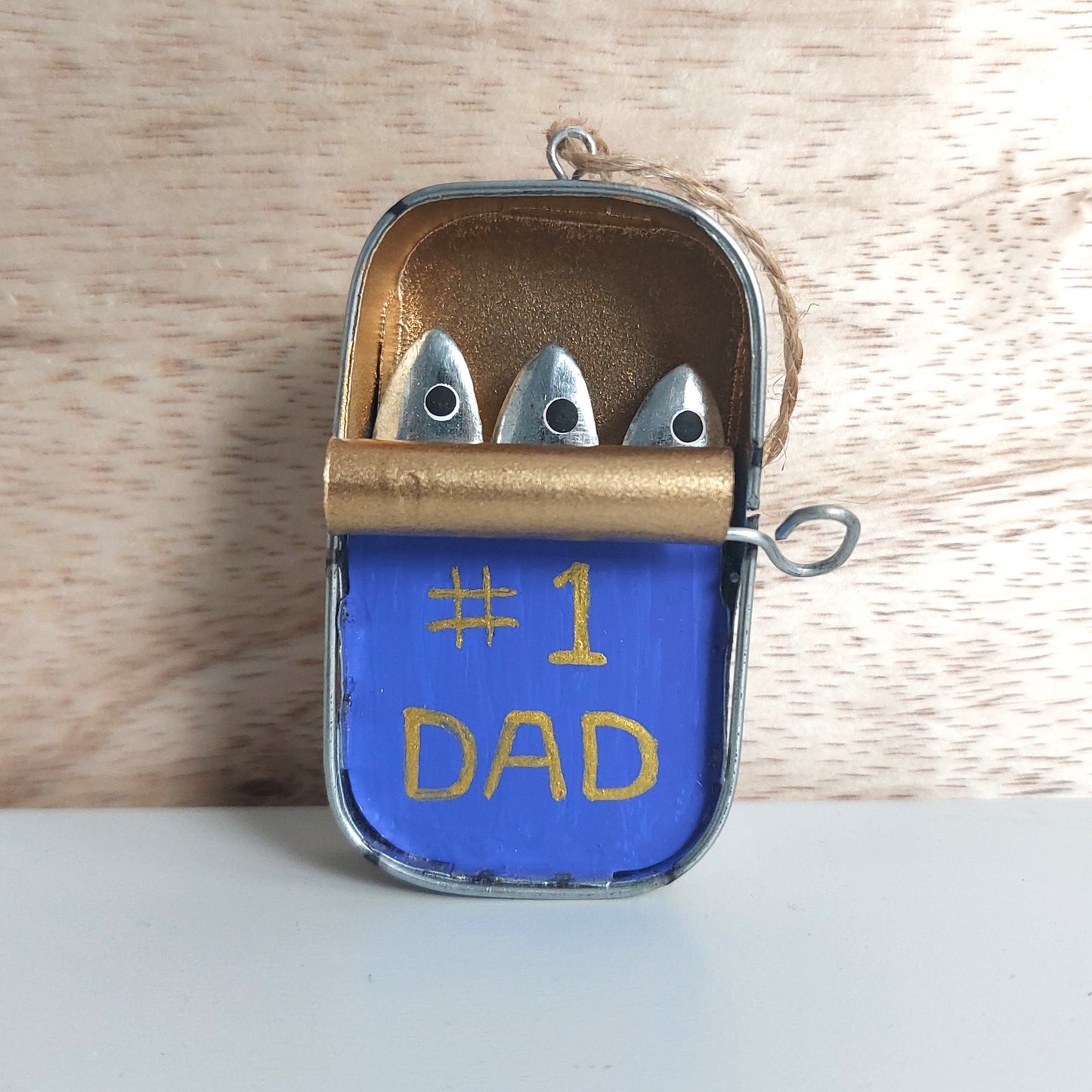 Small metal hand painted decorative tin with metal sardines inside and 'Number 1 Dad' text on a wooden background