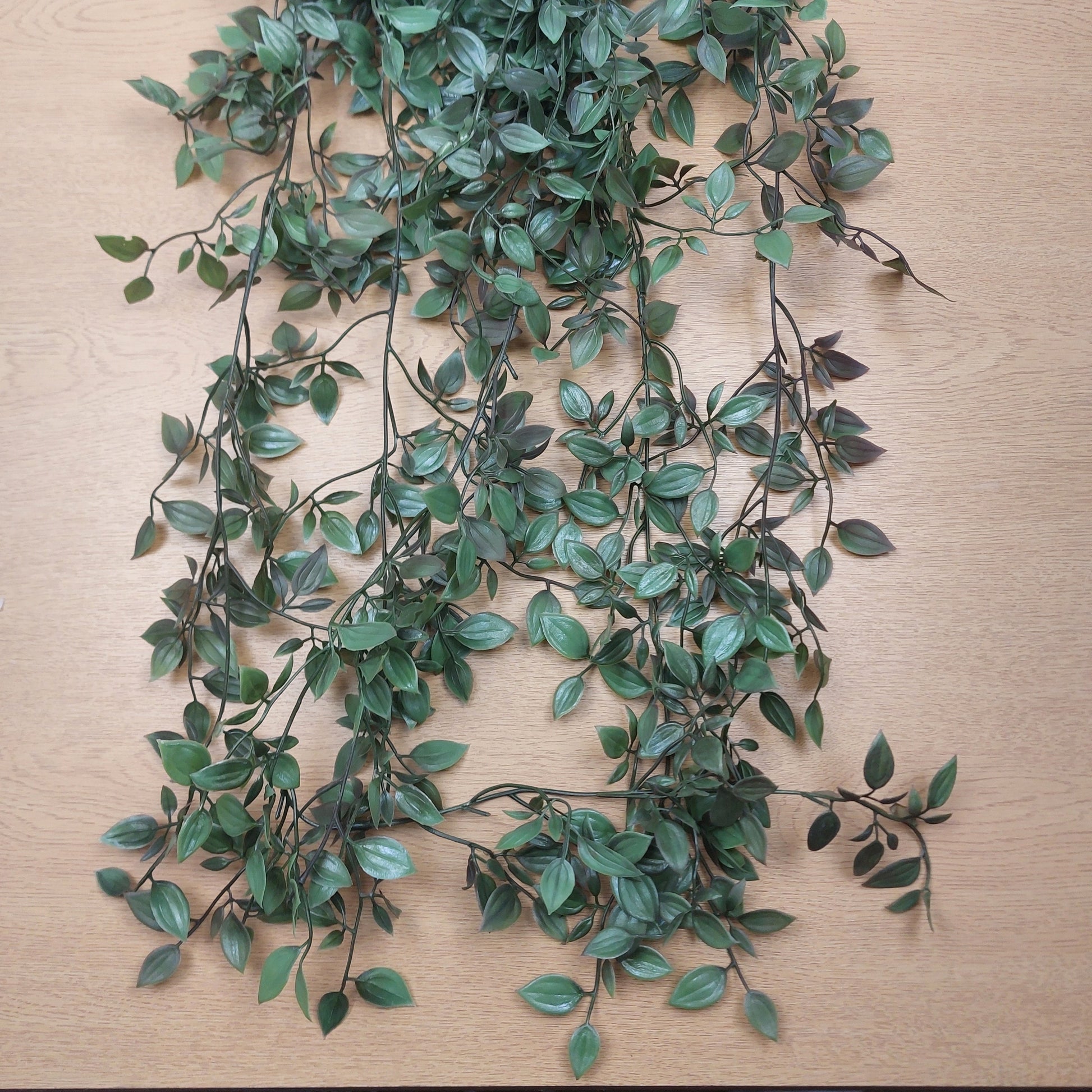 Green leafy artificial ruscus vine garland with dark brown stems laid out on a light wood surface.