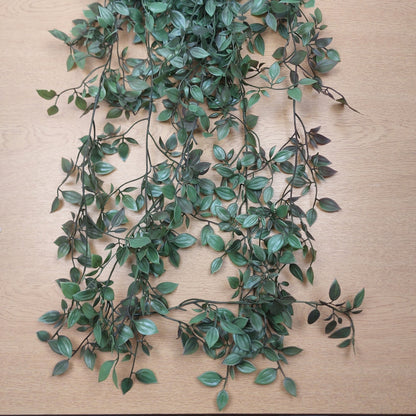 Green leafy artificial ruscus vine garland with dark brown stems laid out on a light wood surface.