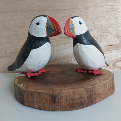 A pair of two wooden hand carved and painted puffins mounted on a wood slice against a pale background