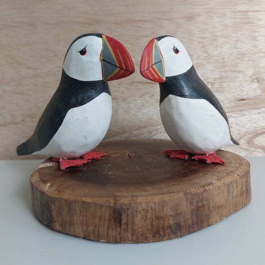 A pair of two wooden hand carved and painted puffins mounted on a wood slice against a pale background