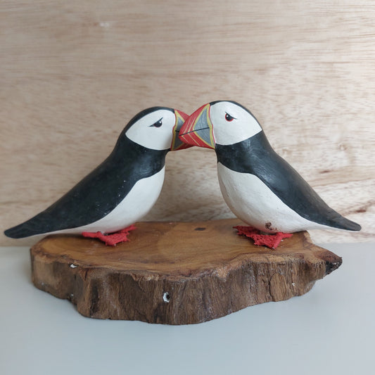 A pair of wooden hand carved and painted puffins on a wood slice base, against a wooden background
