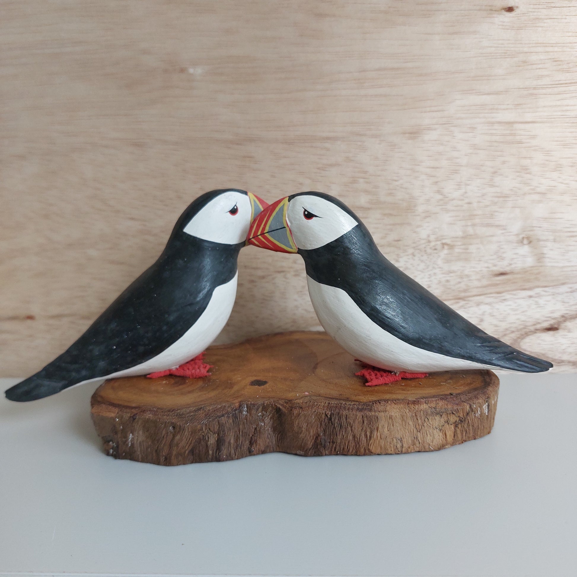Two wooden puffin carvings on a wooden base against a light background
