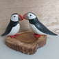 A pair of hand carved and painted wooden puffins mounted on a wood slice against a pale background