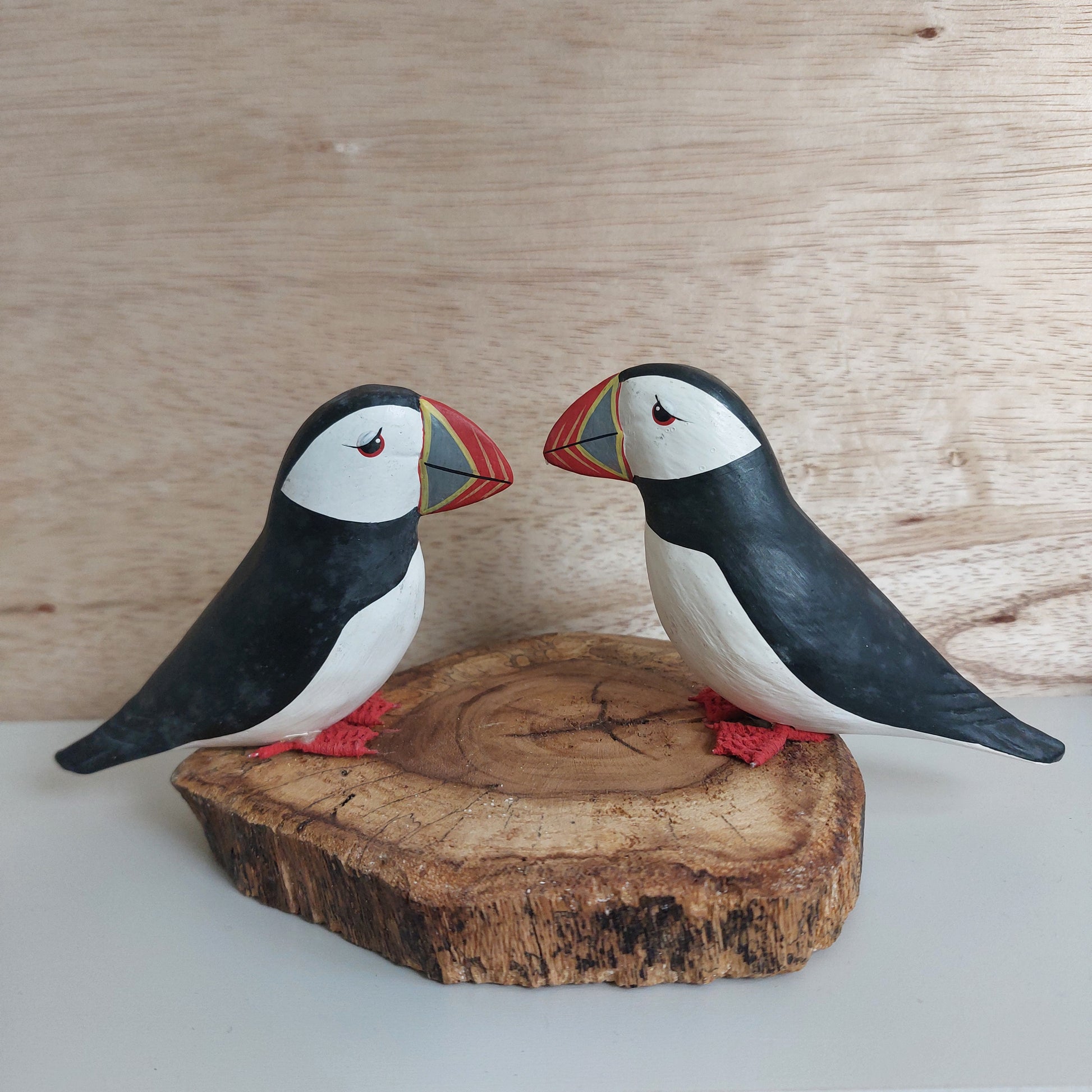 A pair of wooden hand carved and painted puffins mounted on a split wood slice against a pale background