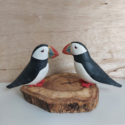 A pair of wooden hand carved and painted puffins mounted on a split wood slice against a pale background