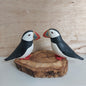A pair of wooden hand carved and painted puffins mounted on a split wood slice against a pale background