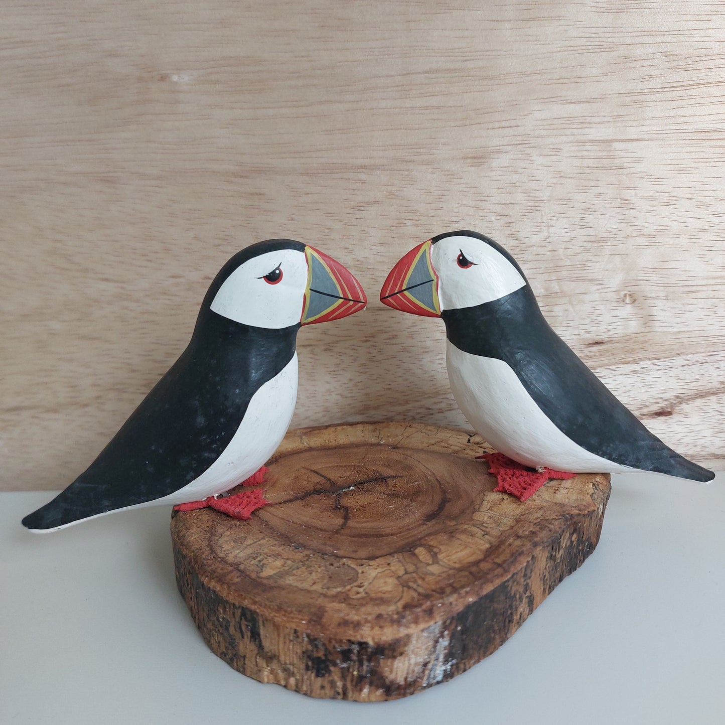 Two wooden decorative puffins on a wooden base against a light wood panel background