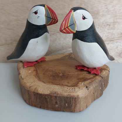 Two hand carved and painted puffin figurines on a wooden base against a neutral background