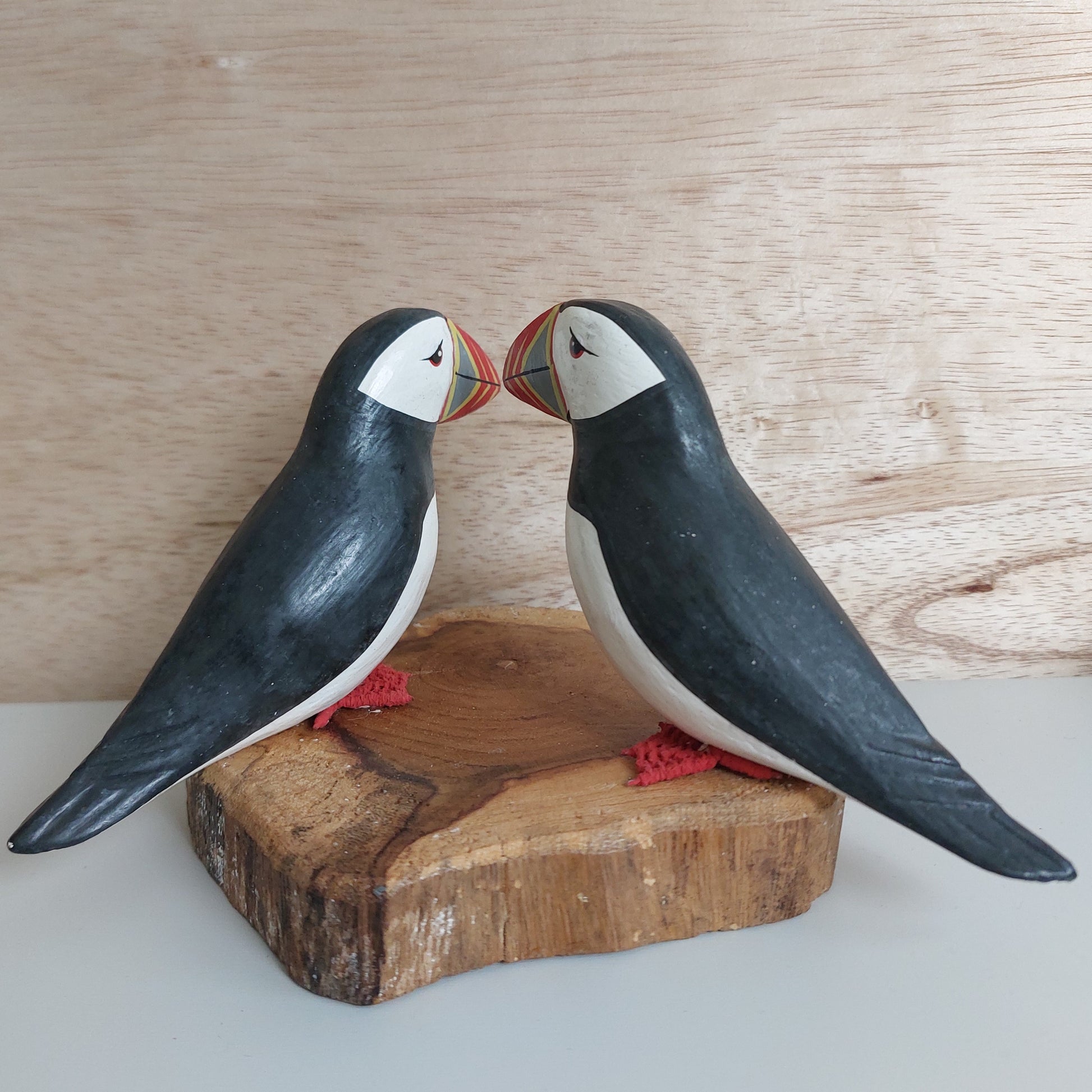 Two wooden handmade puffin figurines on a natural wood base against a wooden background