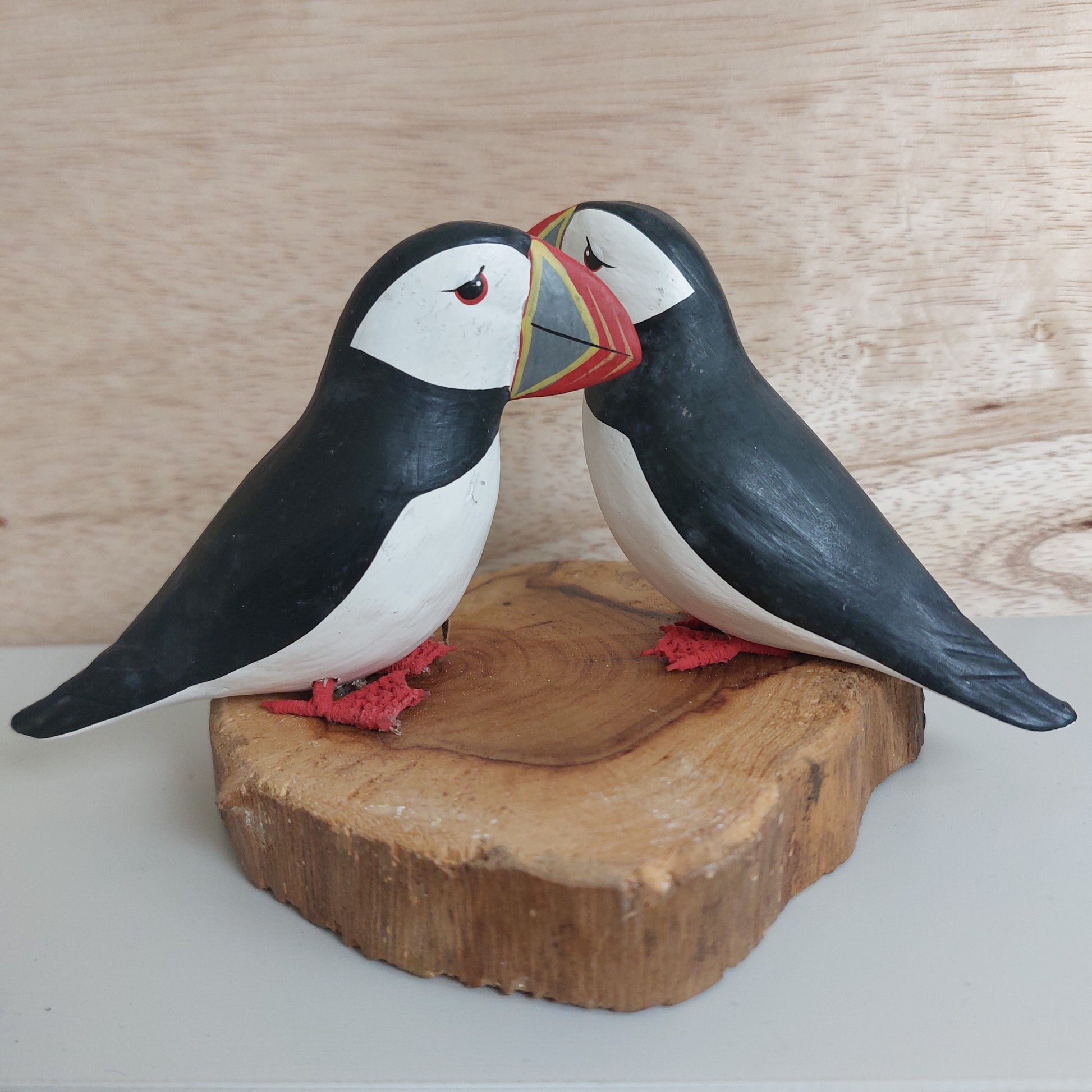Two wooden puffin figurines on a wooden base against a wooden background