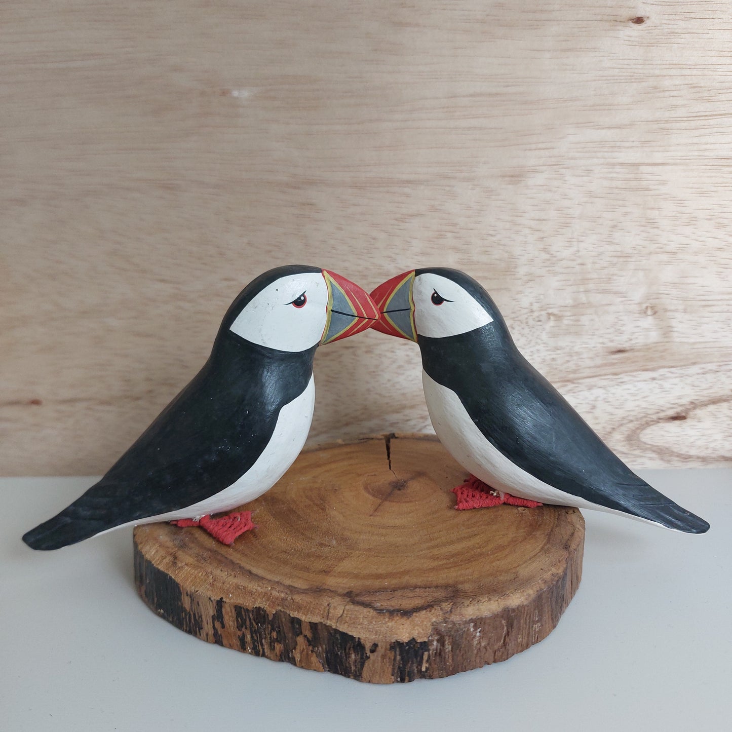 Wooden puffin carvings on a wooden log against a light wood panel background