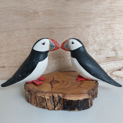 Two handmade painted wooden puffin figurines on a wooden base against a wooden background