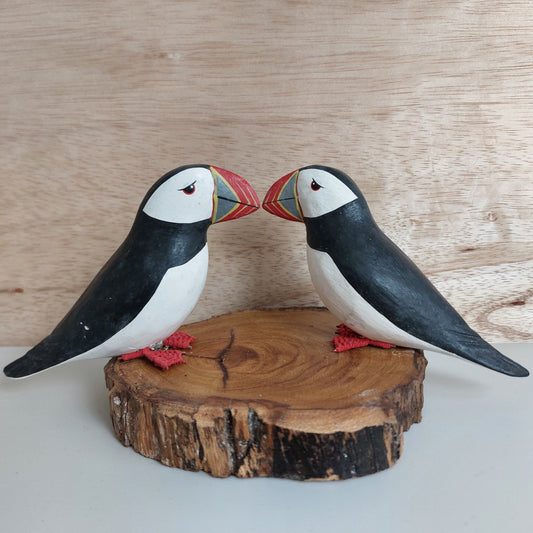 Two handmade painted wooden puffin figurines on a wooden base against a wooden background
