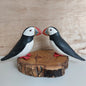 Two handmade painted wooden puffin figurines on a wooden base against a wooden background