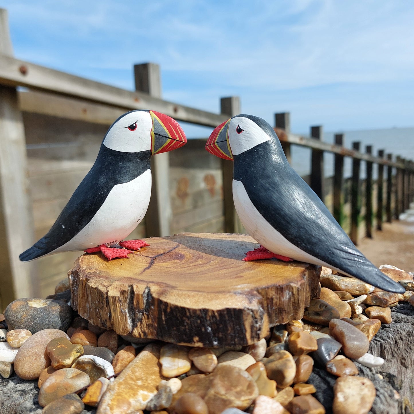 Two wooden hand carved and painted puffin figurines on a wooden block with a beach background