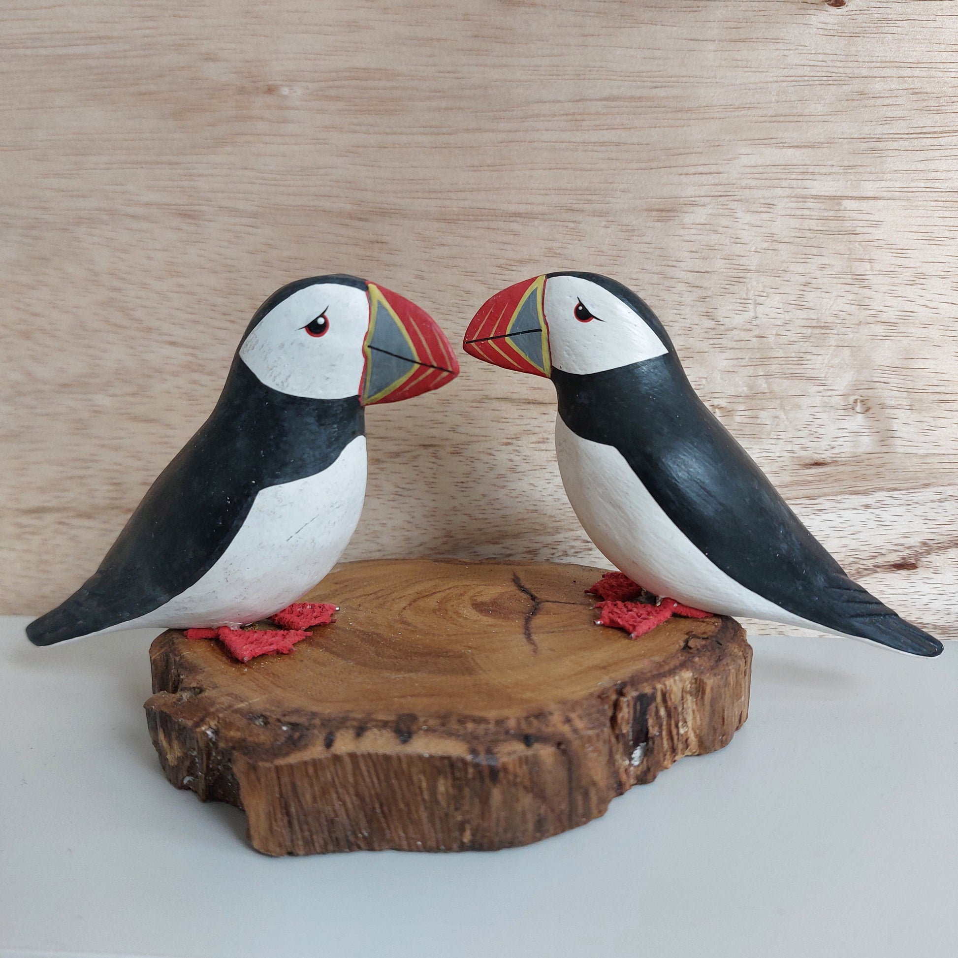 Two hand carved and painted wooden puffin carvings mounted on a piece of driftwood made in Bali on a natural wood background