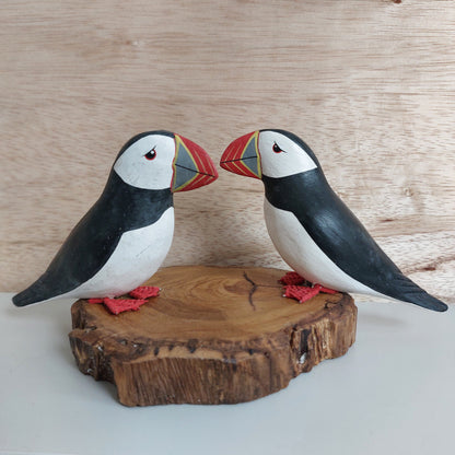 Two hand carved and painted wooden puffin carvings mounted on a piece of driftwood made in Bali on a natural wood background