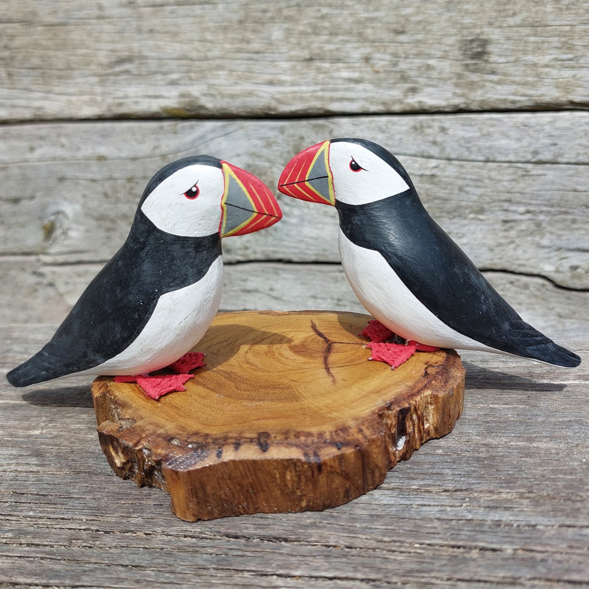 Two wooden hand carved puffin figurines on a wooden base against a wooden background